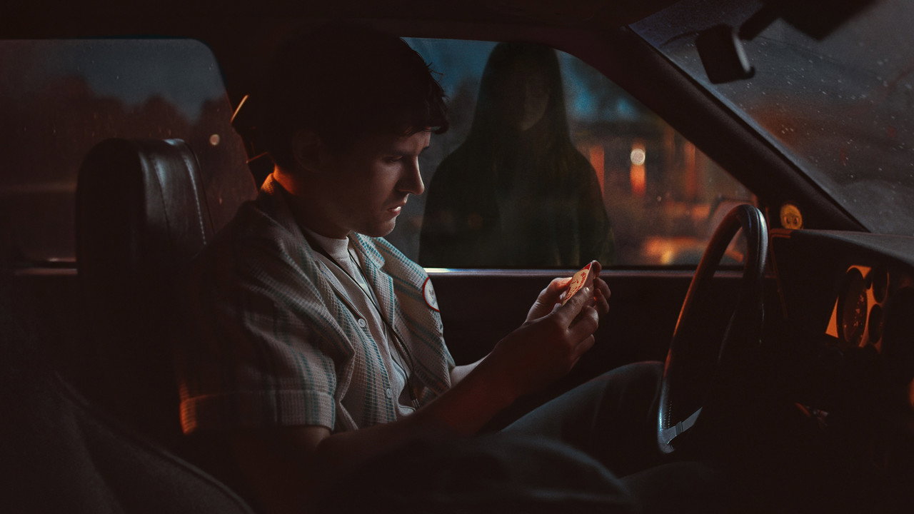 貝爾在車裡低頭看著手中的物件,車窗玻璃映出妮琪的身影